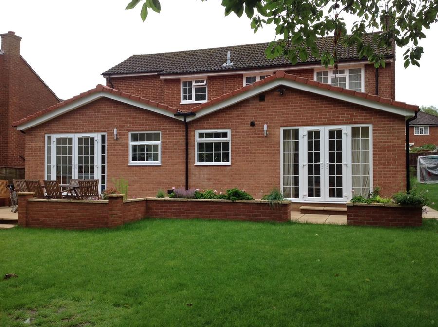 Two storey red brick rear extension with plantation shutters and a paved patio