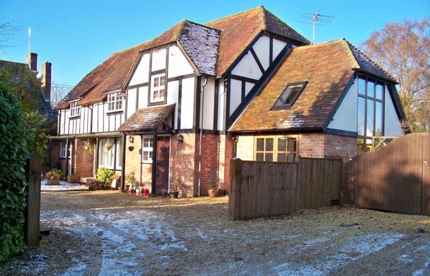 Mock Tudor barn conversion in brick and render with a tiled roof and gabled porch on a gravel drive